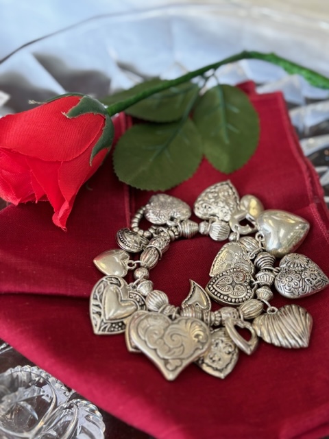 Silver heart charm bracelet on red cloth with a rose